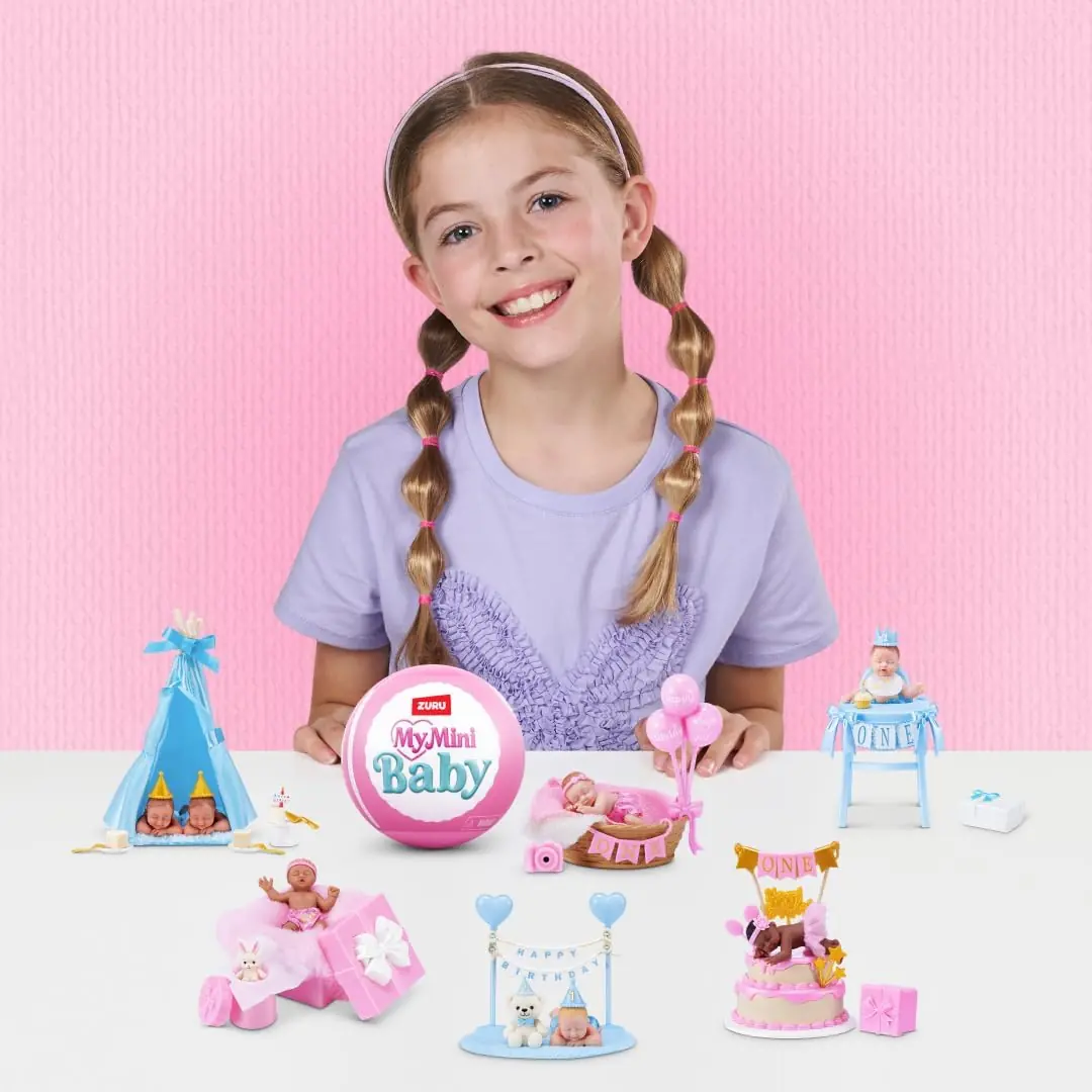Niña con las seis escenas de My Mini Baby Happy Birthday montadas sobre una mesa blanca y la cápsula rosa en el centro
