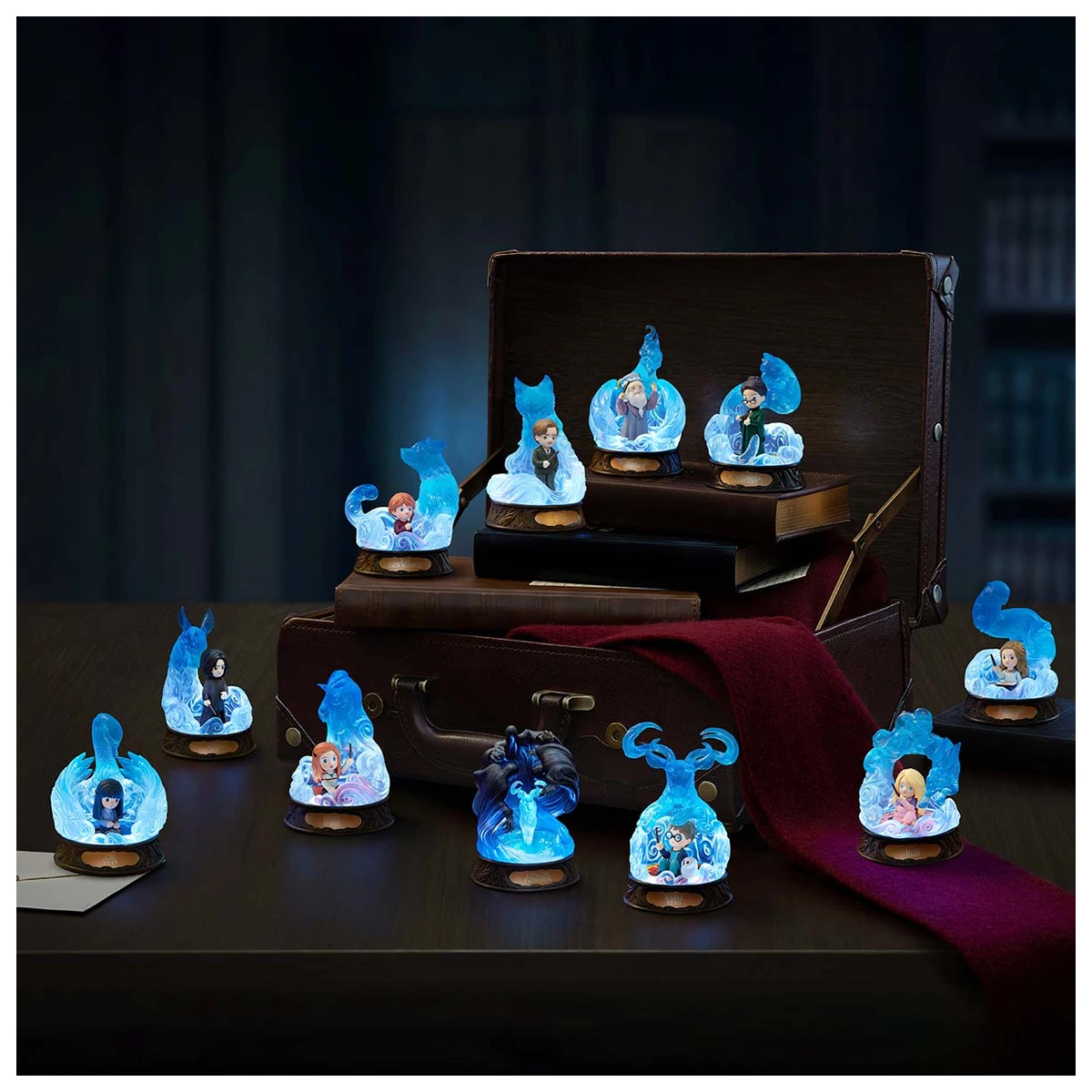 Las once figuras de Harry Potter Patronus Series de POP MART iluminadas sobre una mesa con dos maletas de Hogwarts