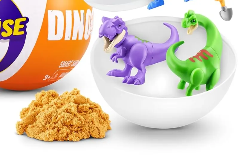 T-rex morado y saurópodo verde dentro de la media cápsula blanca, junto al montón de Smart Sand