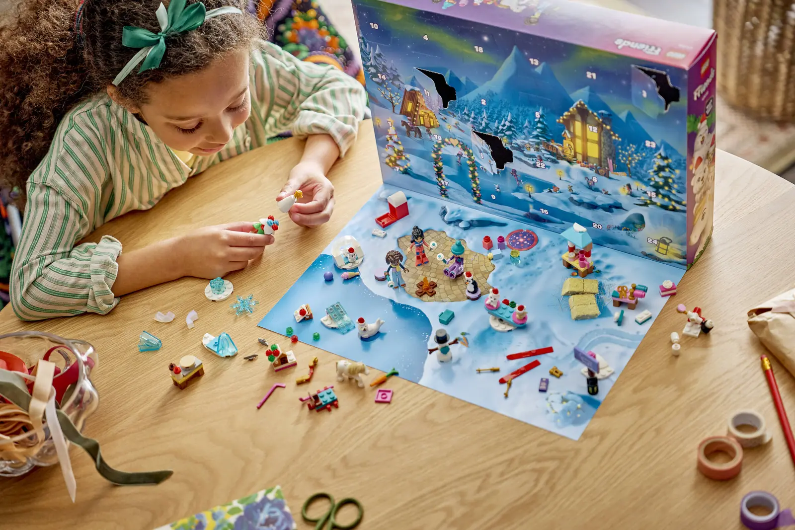 Niña montando el calendario de Adviento LEGO Friends 2026 sobre el tapete nevado de la caja