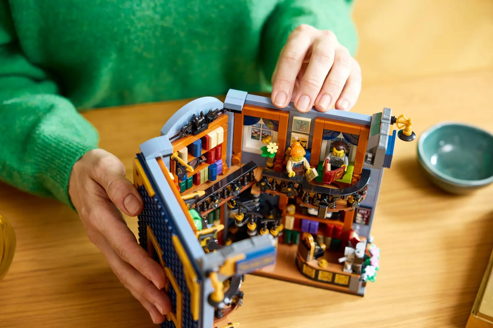 Manos abriendo las alas del LEGO 11379 Rincón entre Libros sobre una mesa de madera